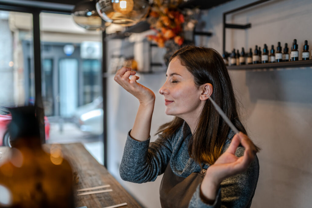 Young Perfumer preparing perfume while sitting at table in her own store