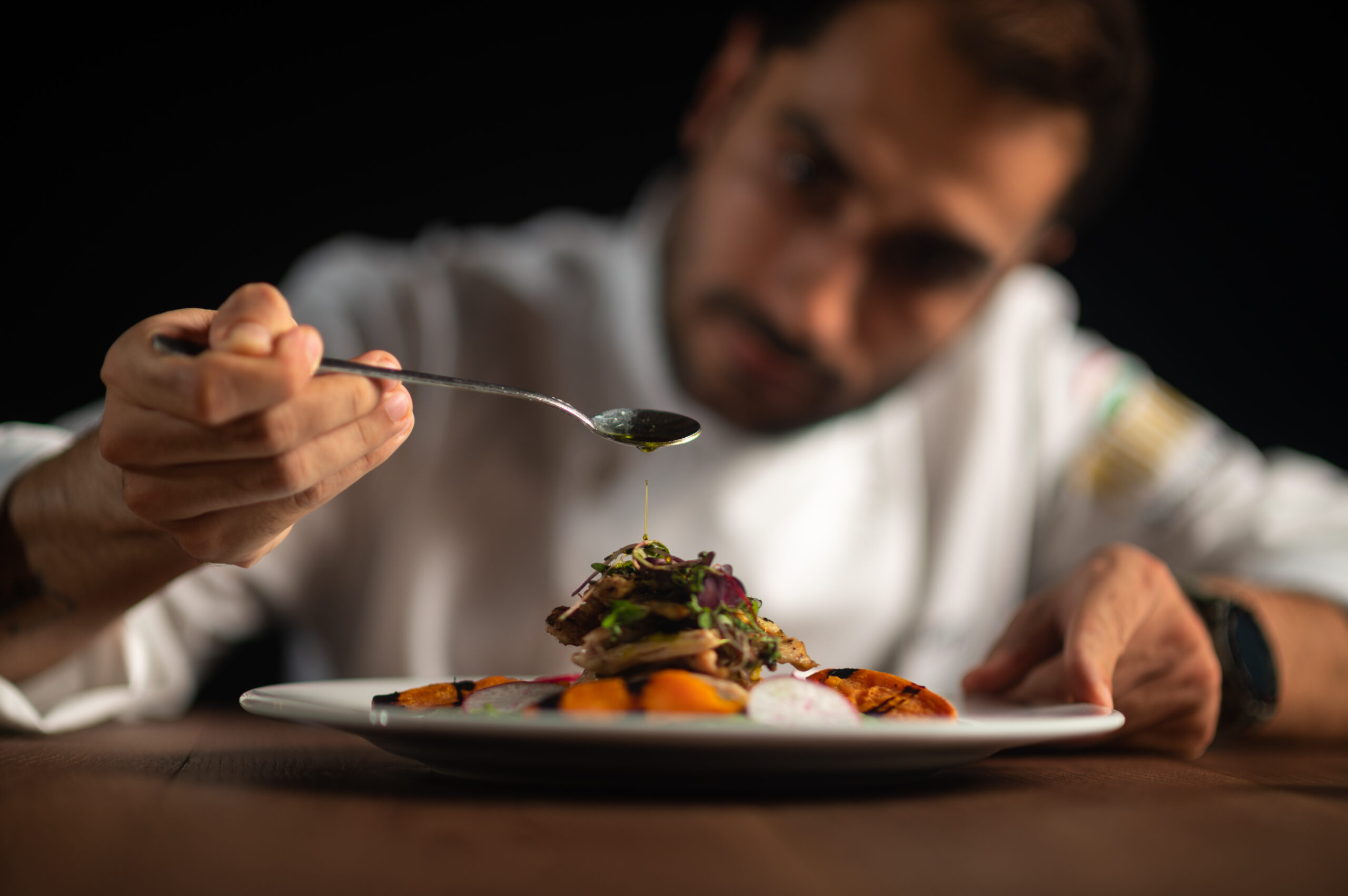 A male chef pouring sauce on meal