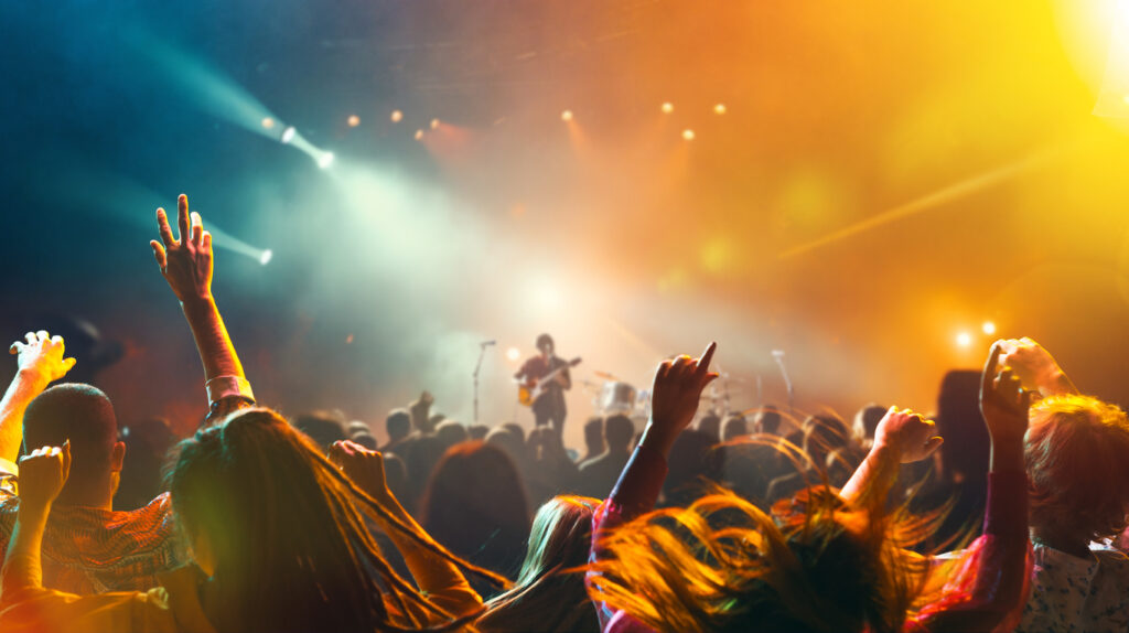 Crowded concert hall with stage, spotlight indoor and people silhouette dancing and singing on dancefloor during summer music festival