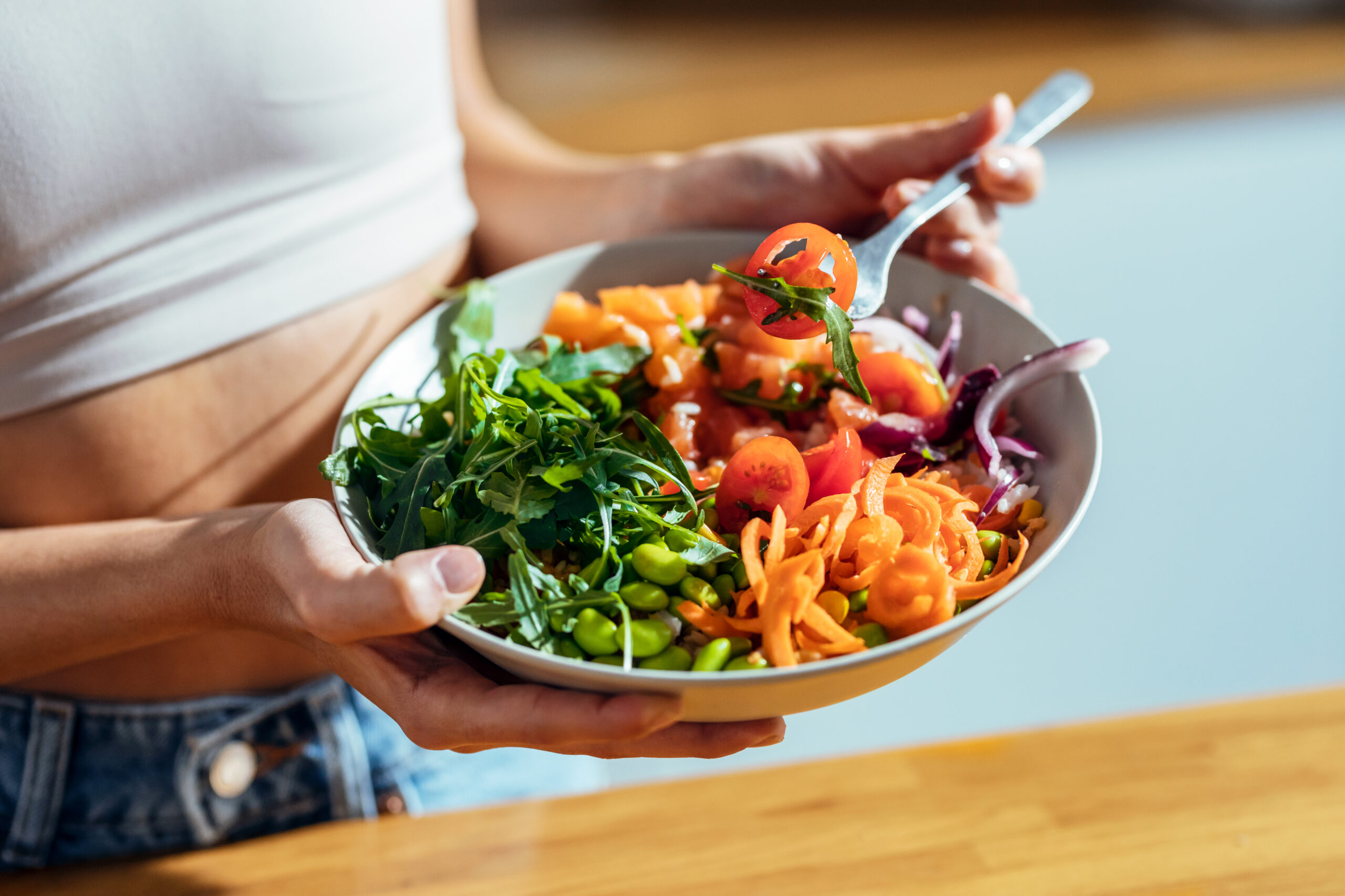 Fitness woman eating a healthy poke bowl in the kitchen at home