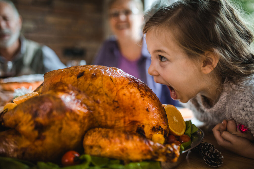 Small girl having fun while about to bite a roasted turkey on Thanksgiving