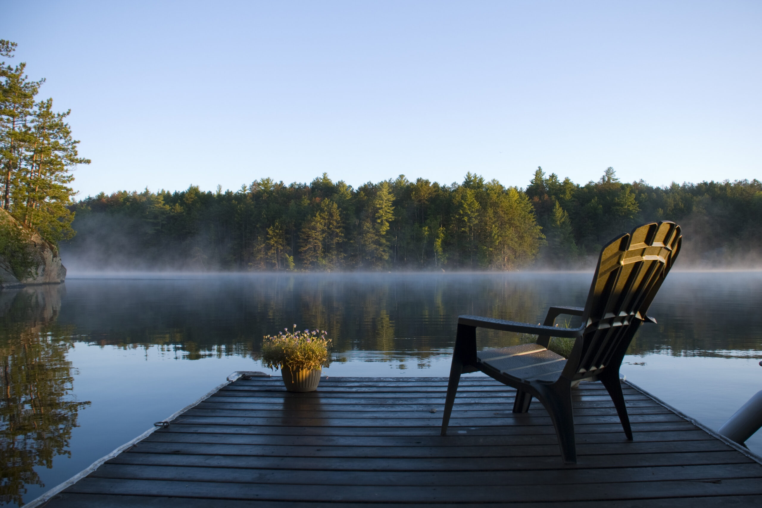 Empty chair overlooking a lake with mist and a forest