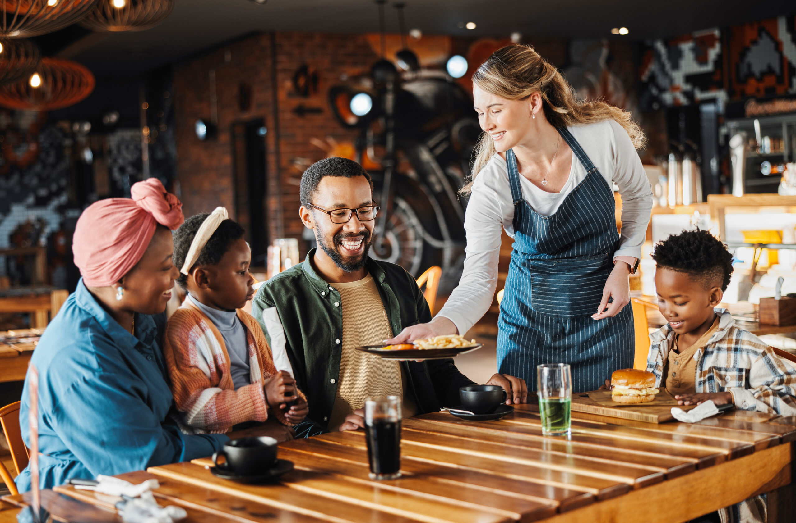 Family, lunch and service of waiter at restaurant with plate, fun and eating at diner together Customer, table and server at cafe with food for happy African parents, children and relax at gathering