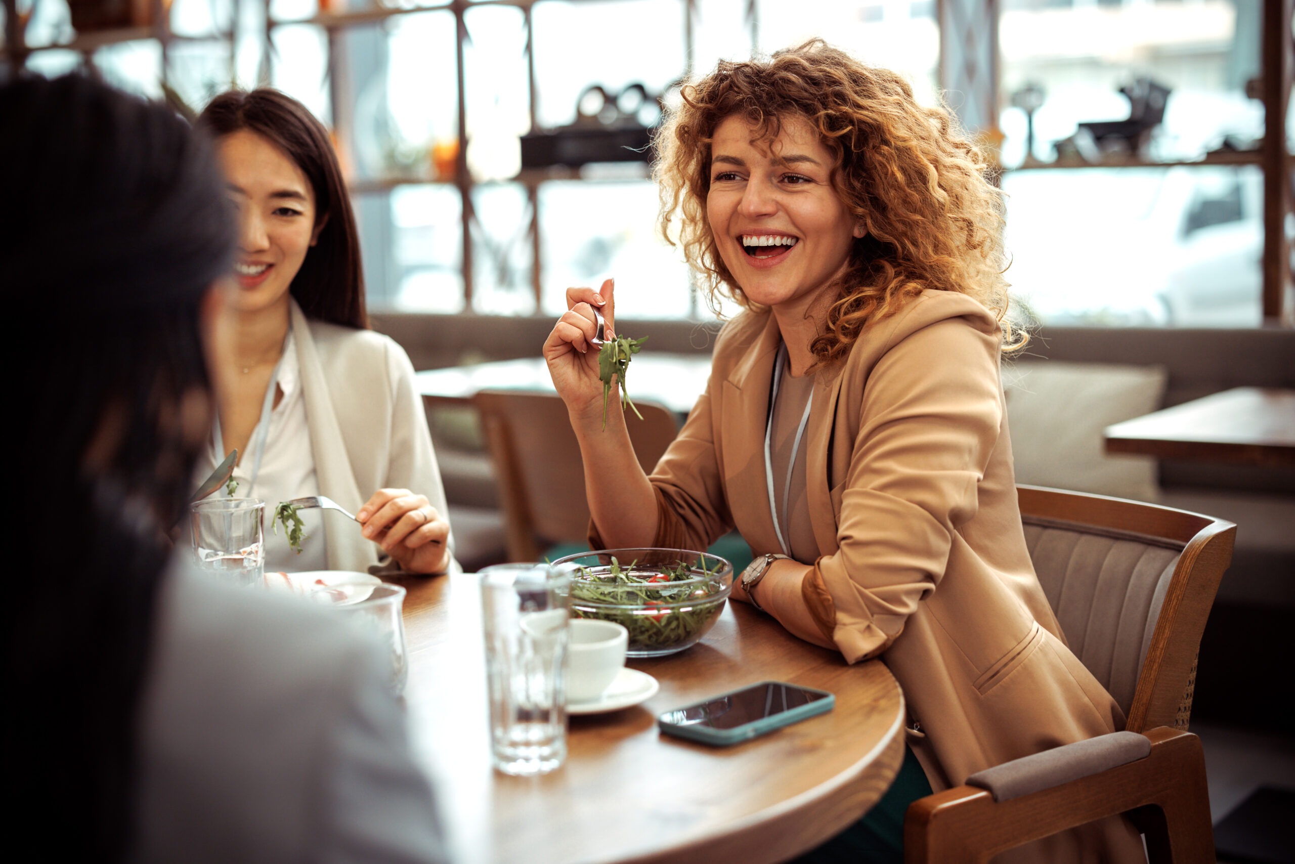 Smiling well dressed businesswoman laughing while having lunch with colleagues at the restaurant